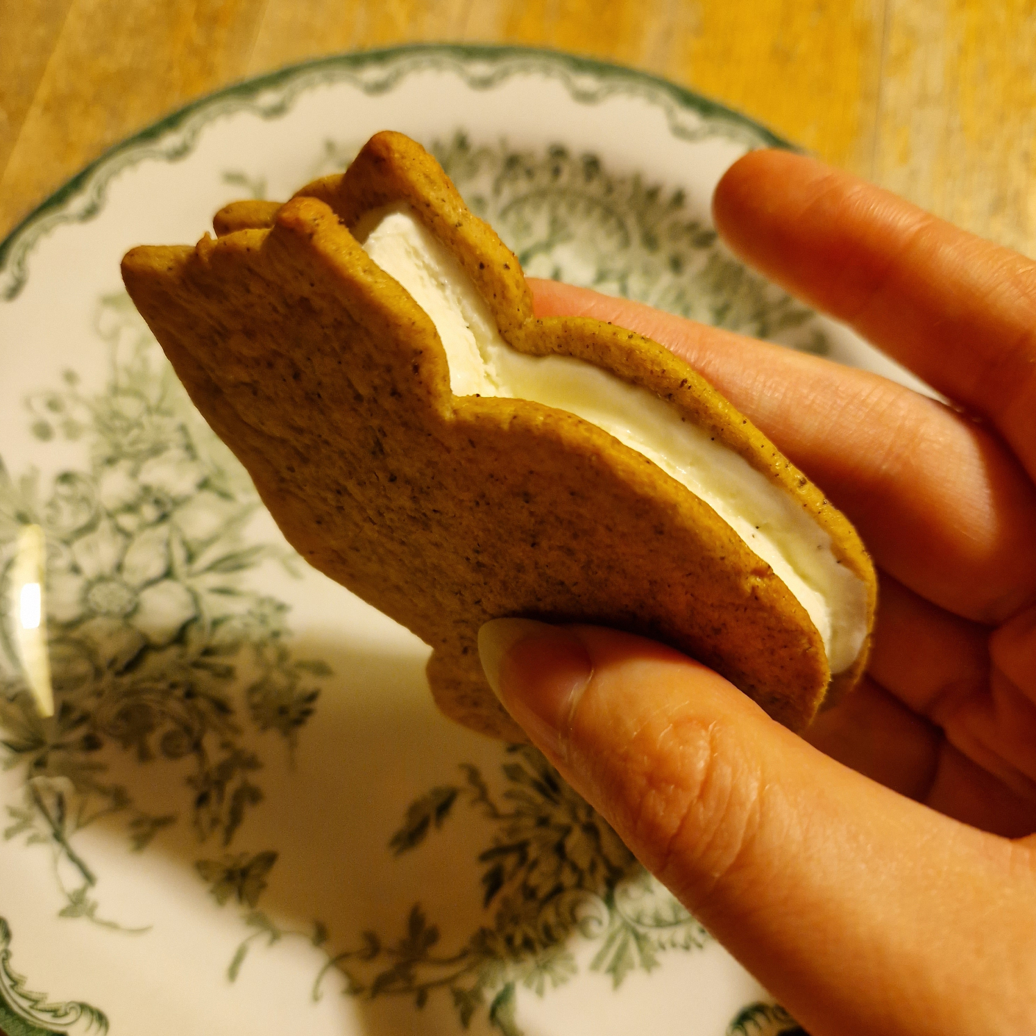 A cat shaped ice cream sandwich held in a hand, a plate in the background.