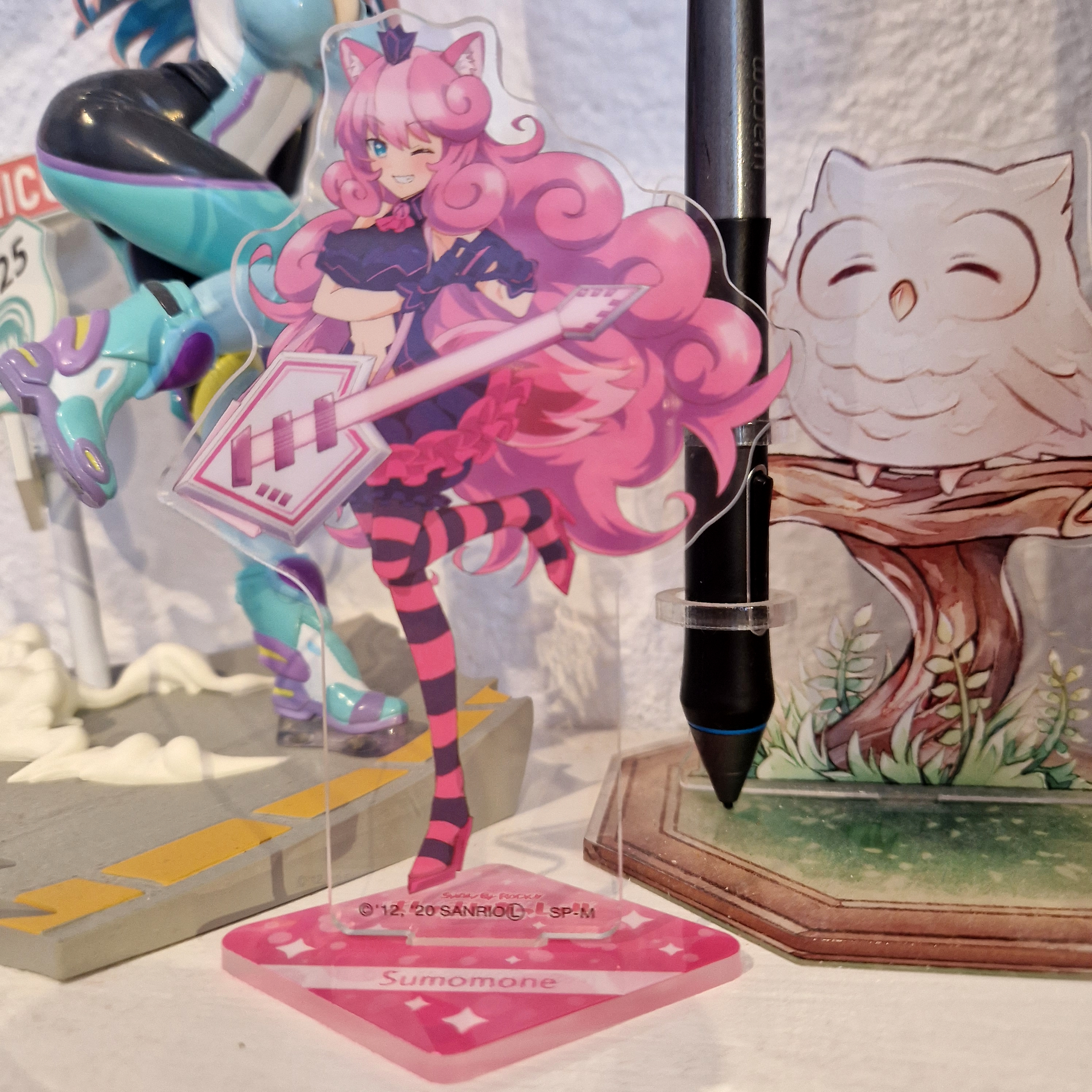 An acrylic stand of Sumomone from Show By Rock, making a heart with her hands and winking.